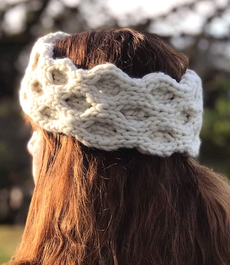 A close up of a woman's head wearing a knitted ear warmer in the honeycomb cable pattern stitch