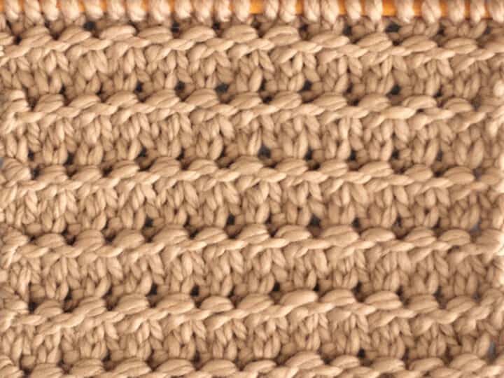 Knitting Swatch in the Granite Stitch Pattern texture in light brown yarn on a wooden bamboo knitting needle.