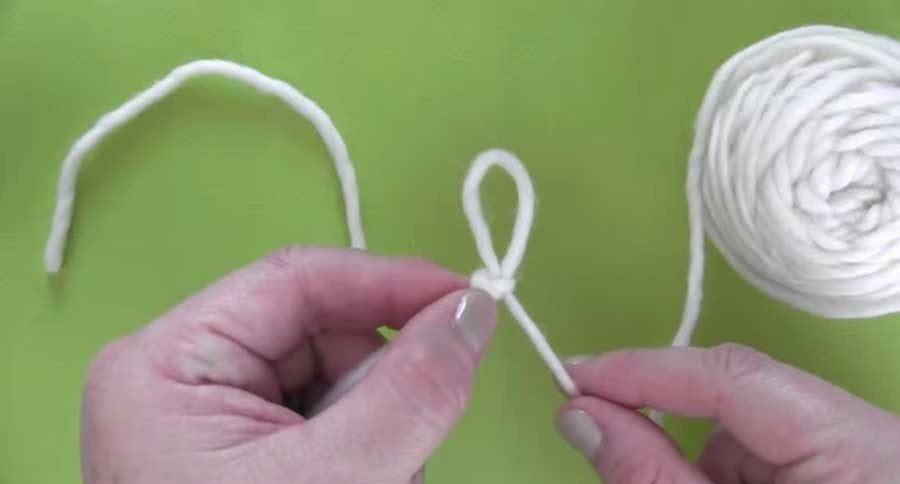 Hands holding a slip knot with white yarn on a green background