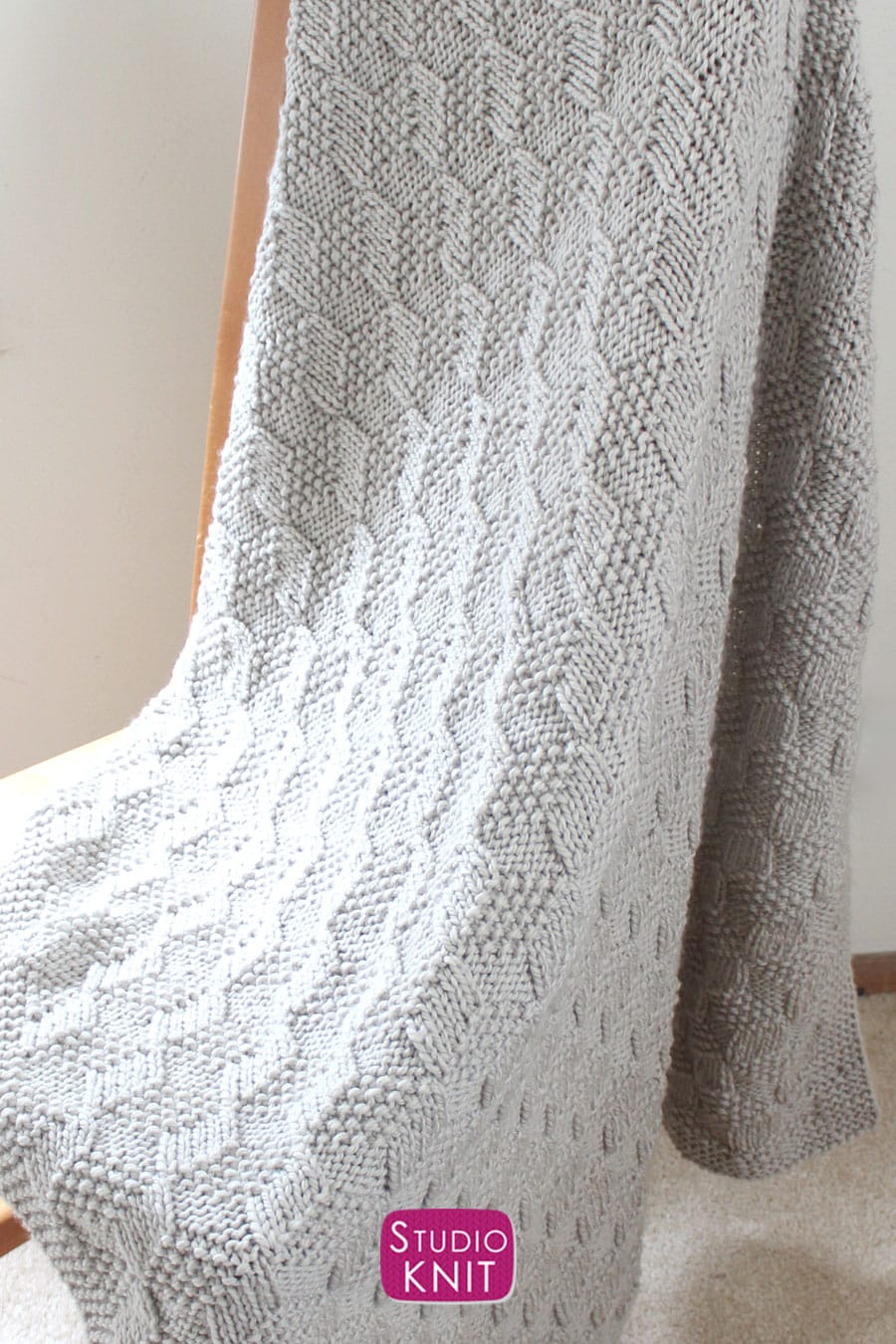 Knitted Blanket in Tumbling Moss Blocks Stitch draped over wooden chair