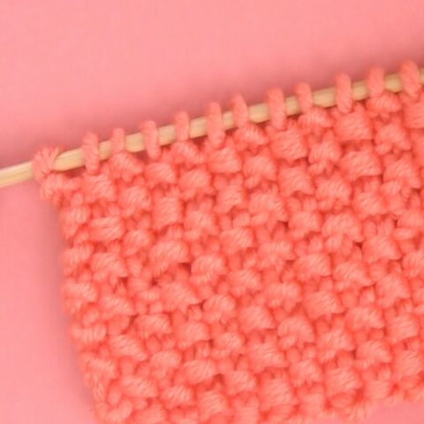 Seed stitch swatch knitted in orange color yarn on knitting needle.