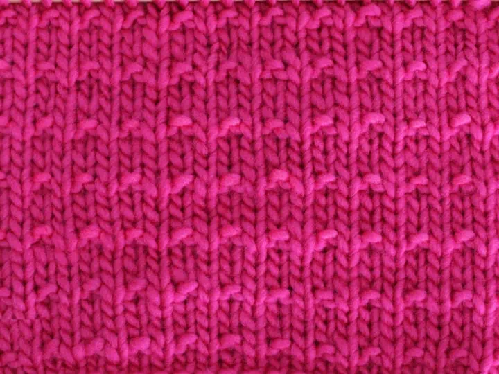 Andalusian Knit Stitch Pattern texture in pink color yarn on knitting needle.