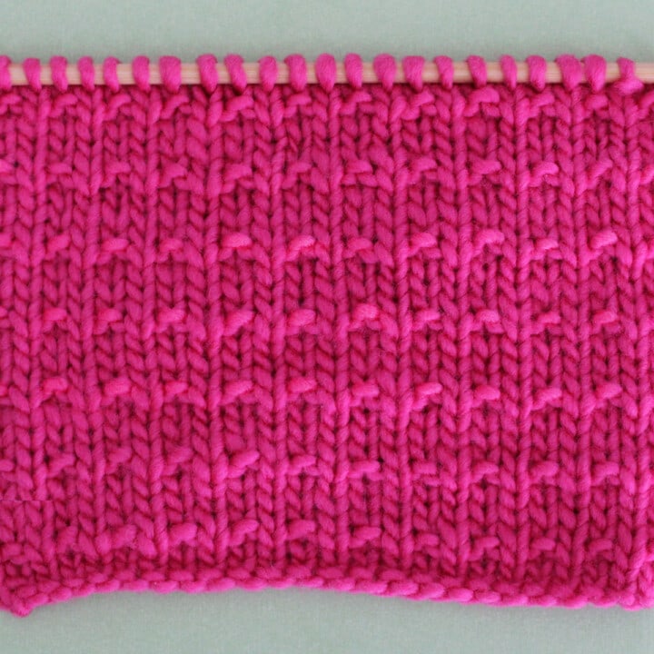 Andalusian Knit Stitch Pattern texture in pink color yarn on knitting needle.