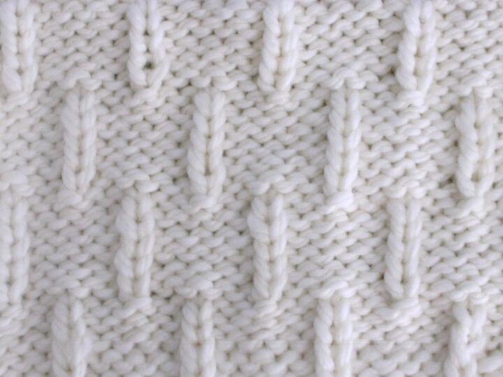 Caterpillar Knit Stitch Pattern in white yarn on knitting needle.