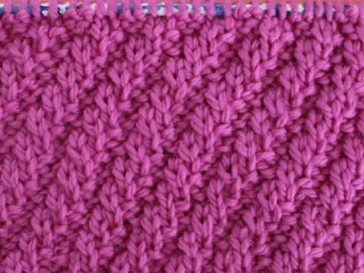 Diagonal Rib Cable Knit Stitch Pattern texture in pink color yarn on knitting needle.