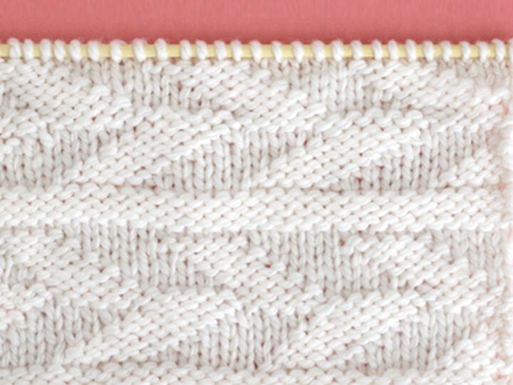 Knitted Embossed Leaf Stitch Pattern in white yarn on knitting needle.