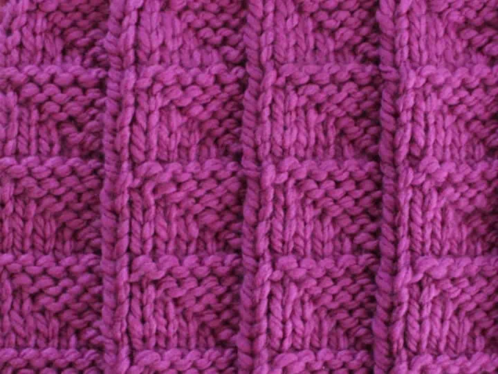 Knitted Flag Stitch Pattern in purple yarn on knitting needle.