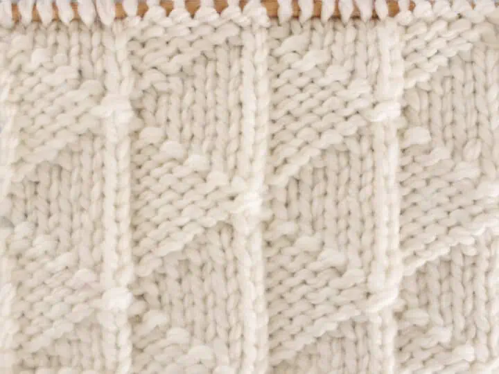 Pennant Pleating Knit Stitch Pattern in white yarn on knitting needle.