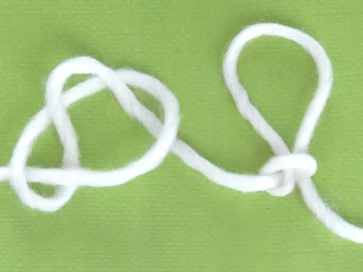 White yarn demonstrating the Slip Knot technique atop a green background.