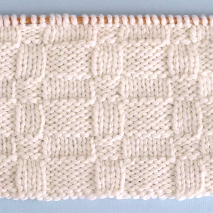 Knitted Wide Basket Weave Stitch Pattern in white yarn on knitting needle.