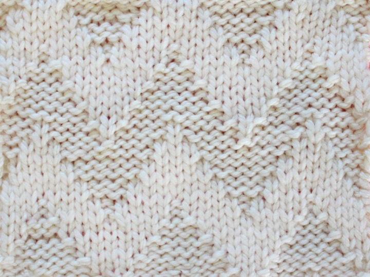 Knitted Wide Chevron Stitch Pattern in white yarn on knitting needle.