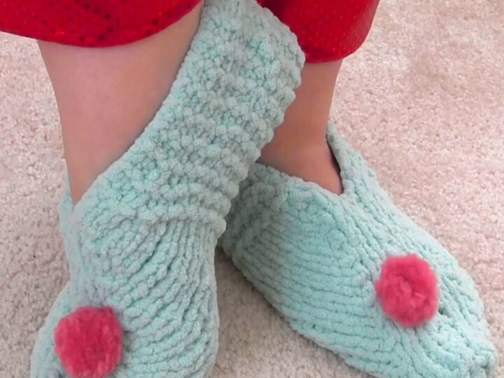 Knitted slippers in light blue yarn color with pink pom poms.