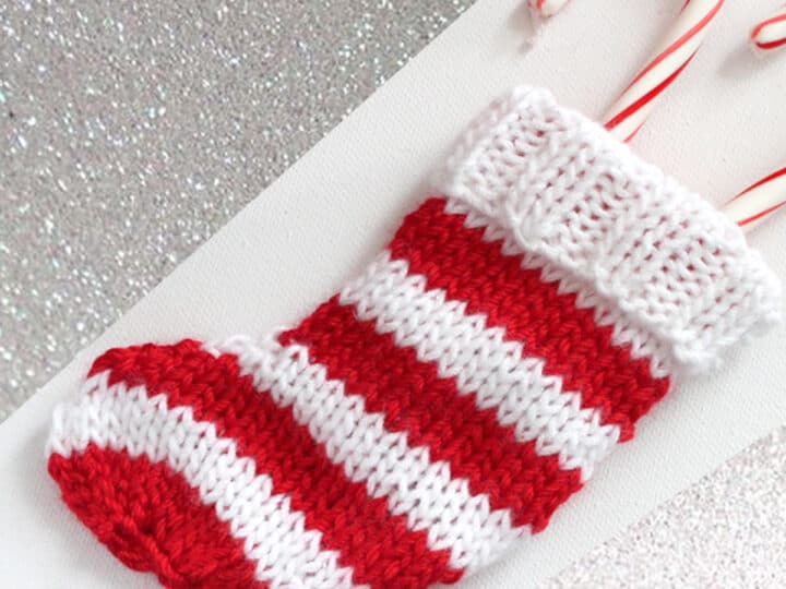 Knitted mini Christmas Stocking in alternating horizontal stripes in red and white yarn with candy canes inside.