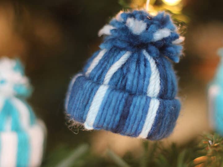 Yarn Hat holiday ornament in blue and white stripes hanging with Christmas tree.