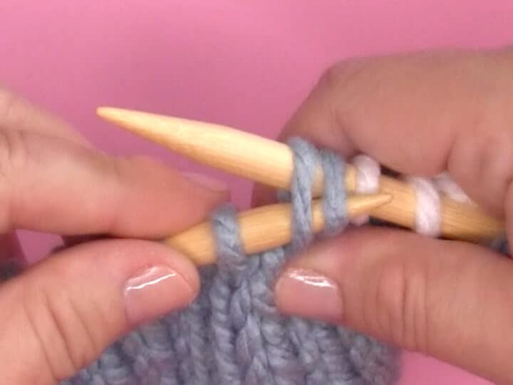 Demonstration of hands SSK knitting decrease technique with needles and yarn.