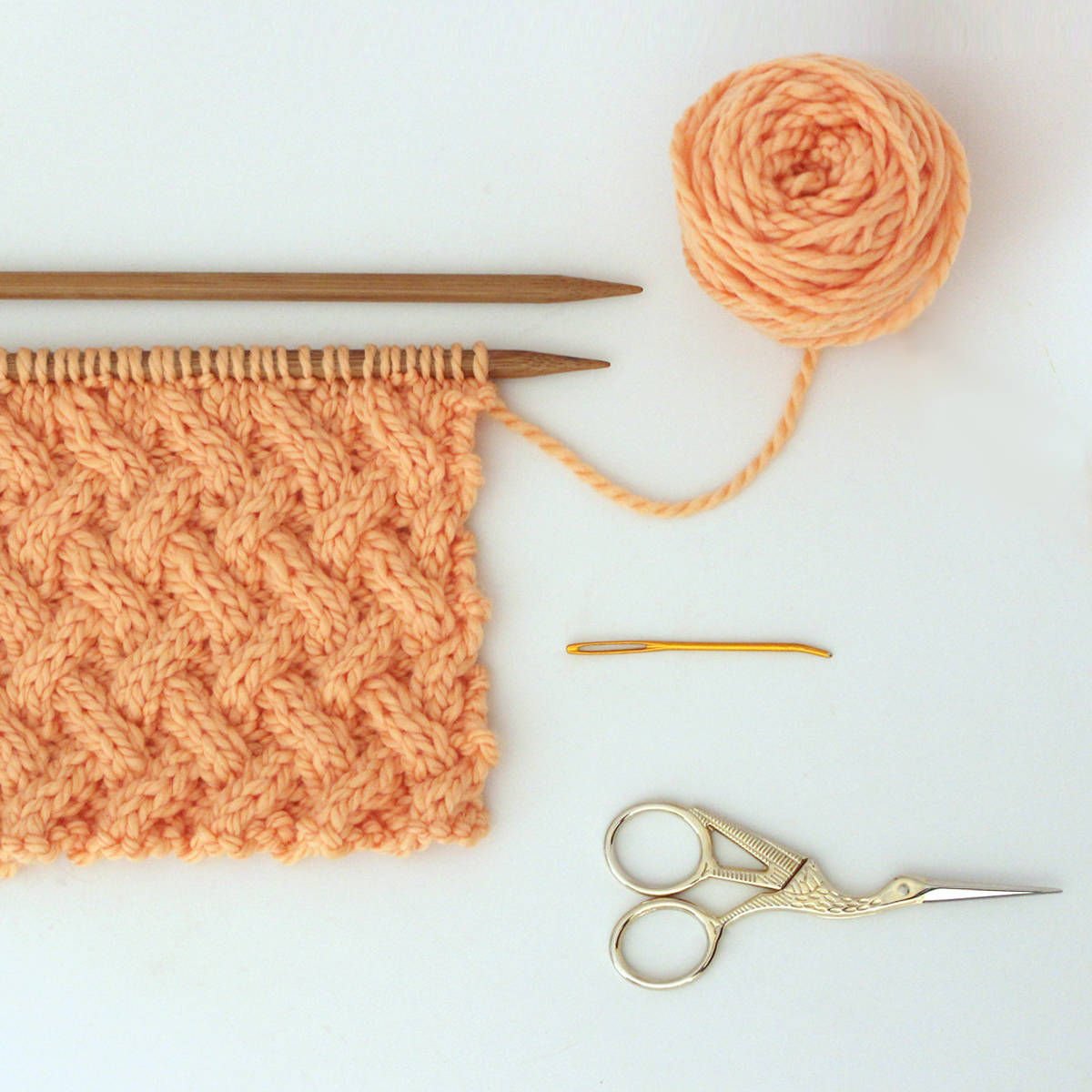 Knitting supplies for Lattice Cable Stitch with yarn, needles, scissors, and tapestry needle.