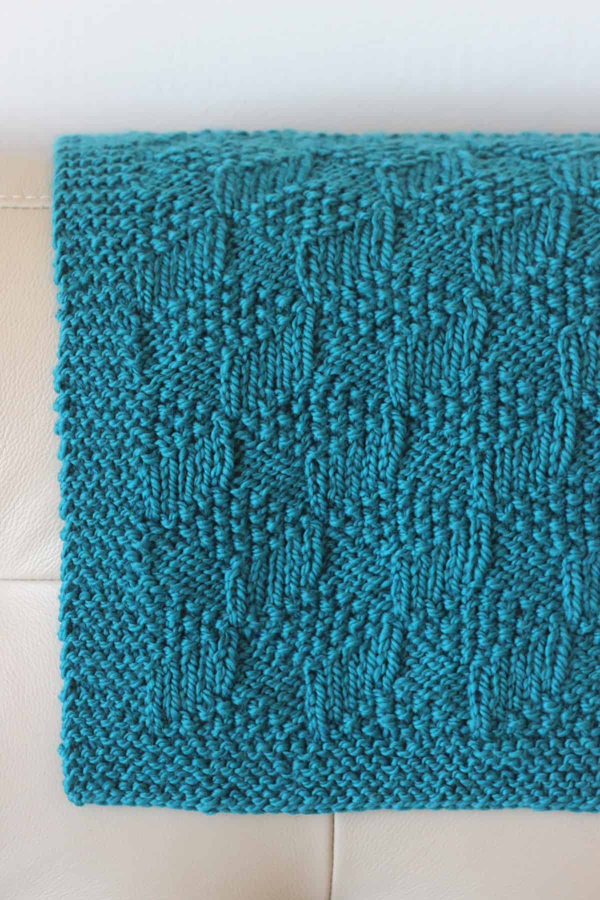 Blue knitted blanket draped on couch in tumbling blocks pattern.