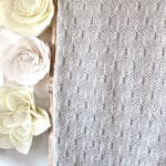 Tumbling Blocks blanket on ladder in light beige yarn color with felt flowers on the wall.