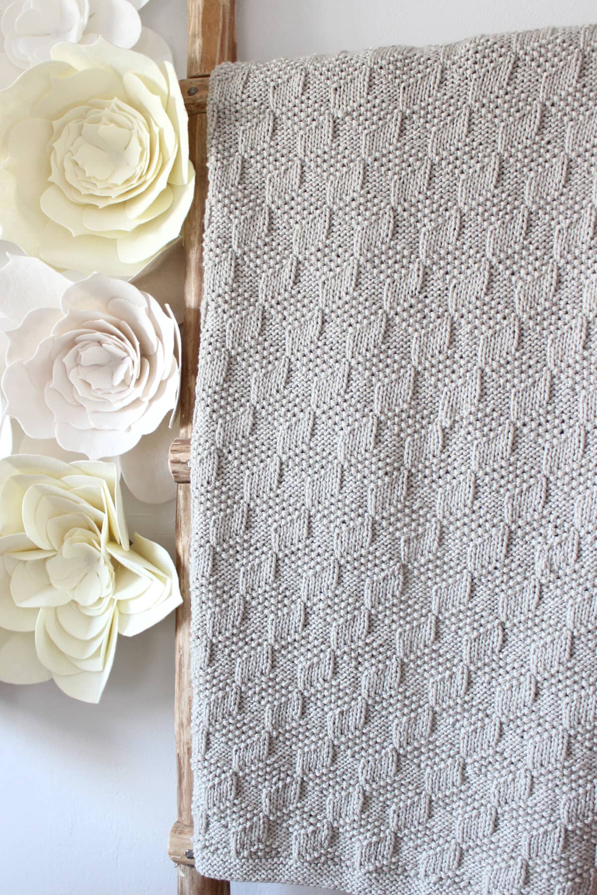 Tumbling Blocks blanket on ladder in light beige yarn color with felt flowers on the wall.