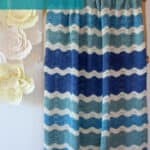 Knitted blanket in ripple wave stitch pattern in shades of blue and white displayed on a wooden ladder.