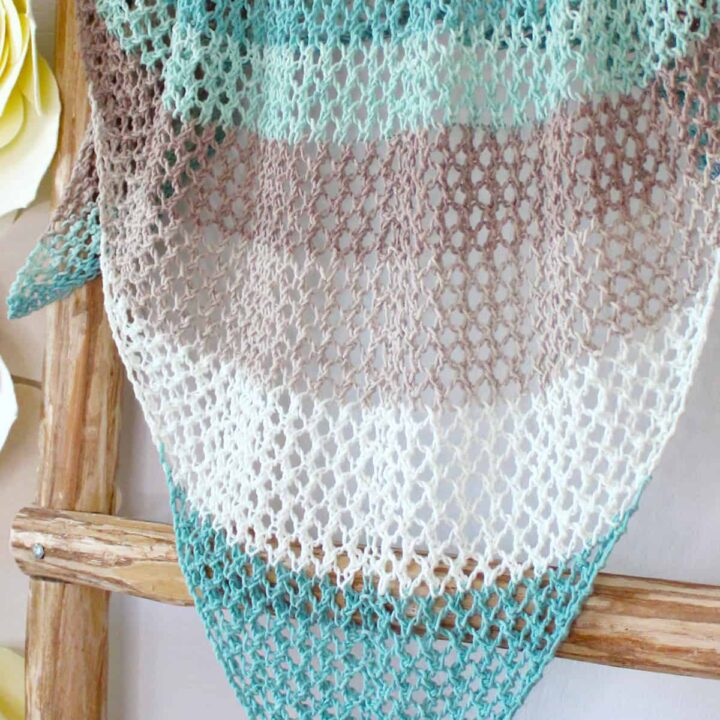 Mesh knitted shawl in multicolors displayed on a wooden blanket ladder.