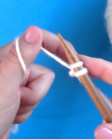 Basic beginners with hands knitting stitches onto a needle with white yarn color.