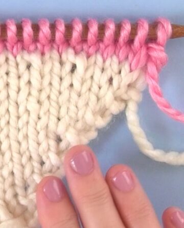 Beyond basics knitting with white and pink knitted triangle shape.