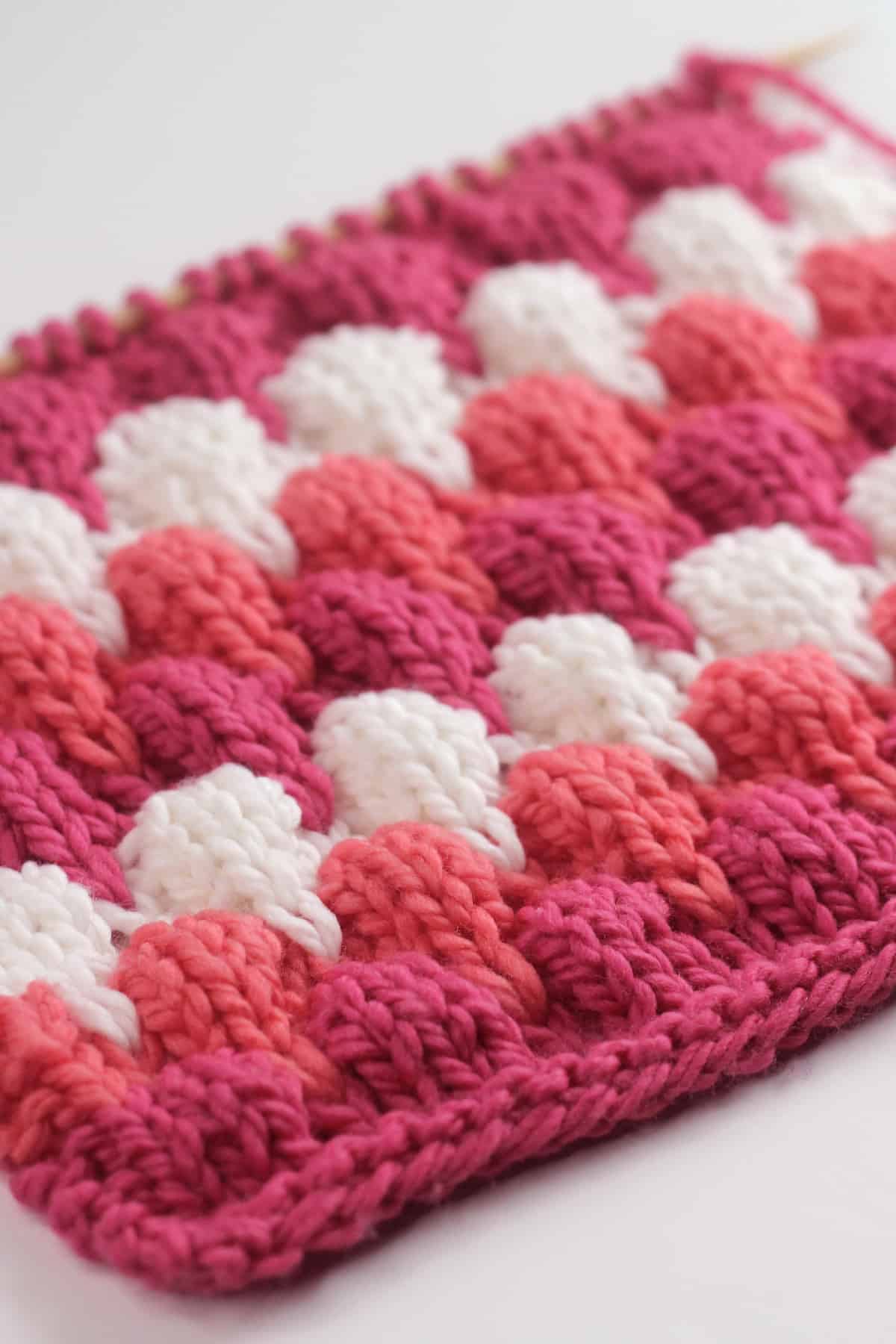 Bubble Stitch knitted texture in pink, orange, and white colored yarn on knitting needle.