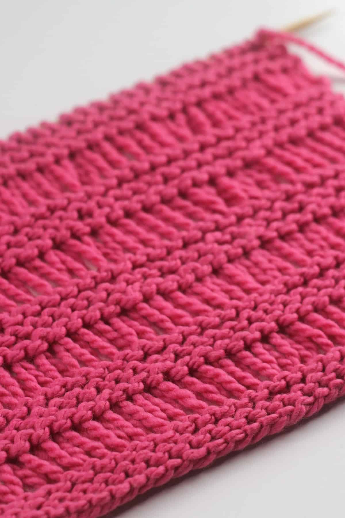 Close-up side view of the Garter Drop Stitch knitting pattern in bright pink yarn color.