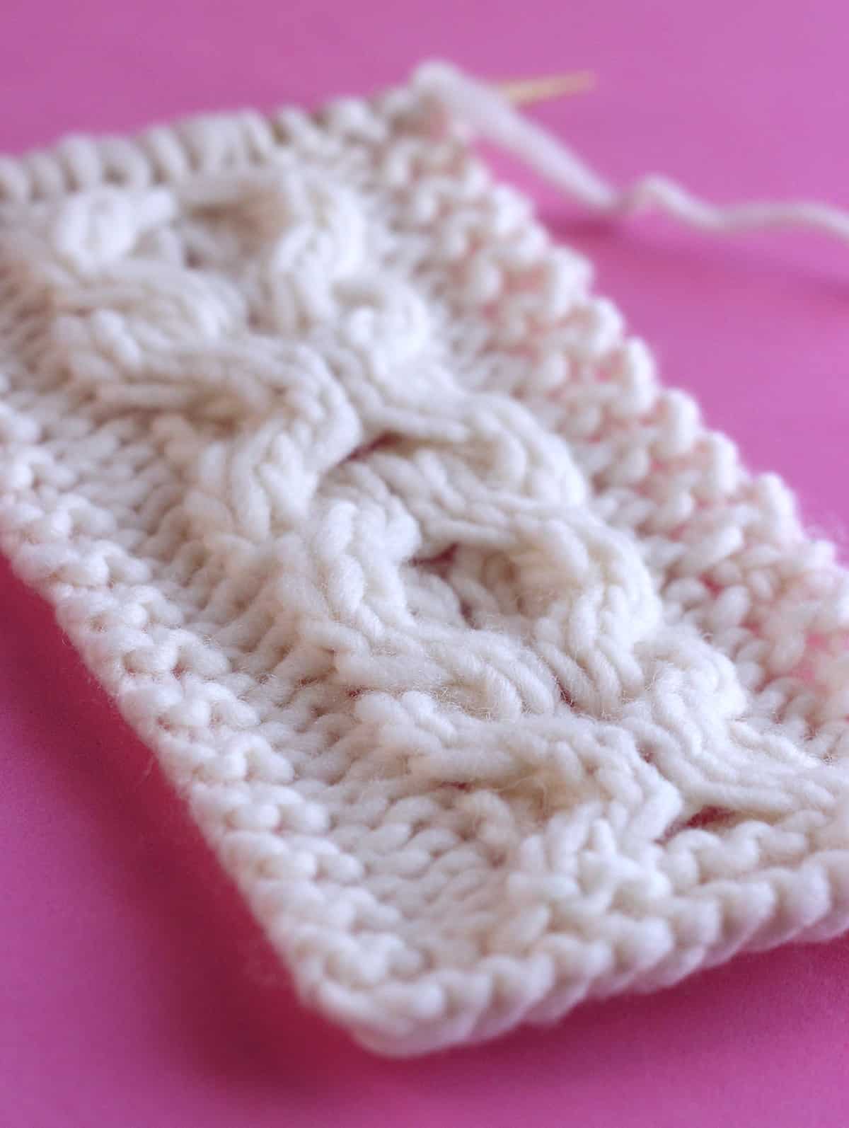 Side view with texture detail of the XO Cable pattern knitted on straight needles with white colored yarn.