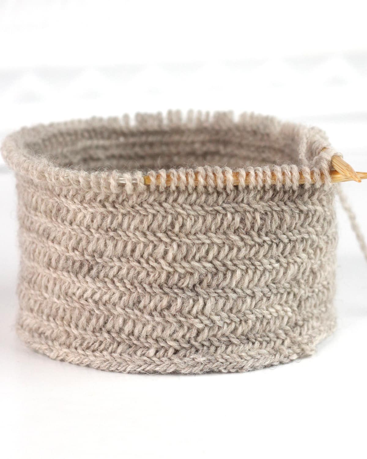 Herringbone knit stitch texture in gray-colored yarn on circular needles.