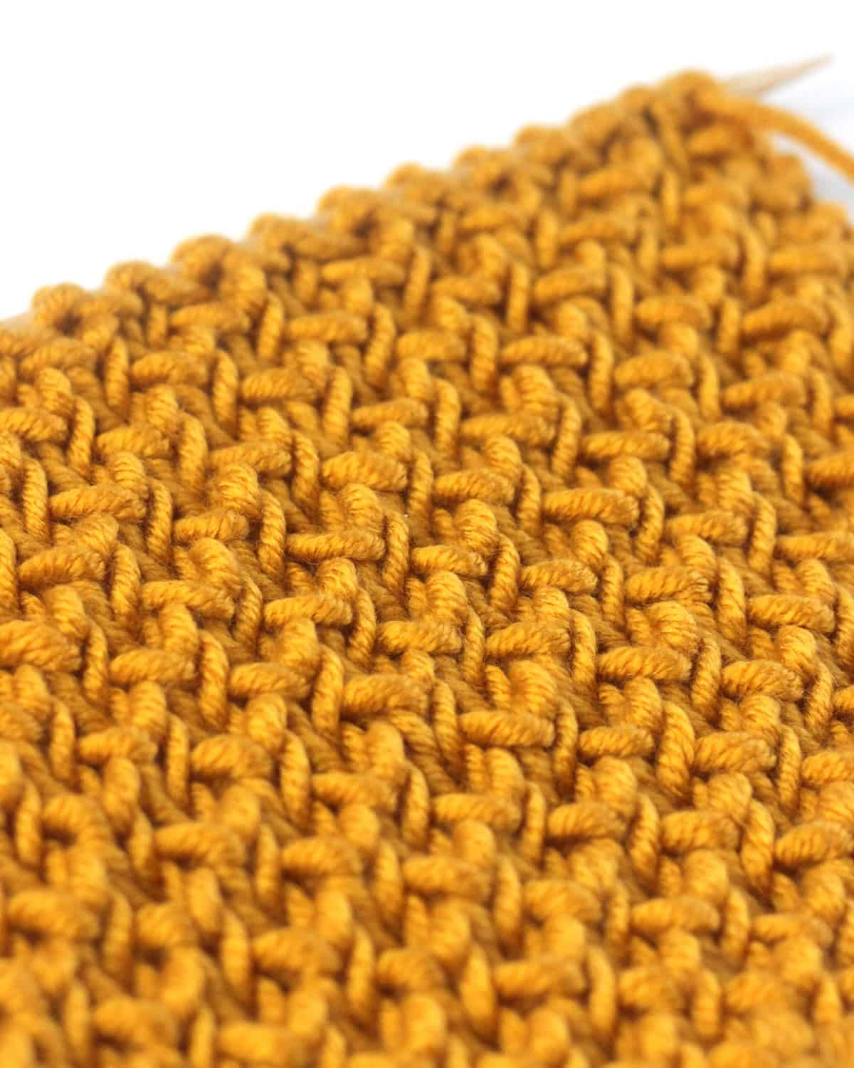 Close-up of Bee stitch brioche knit stitch pattern flat on straight needle in yellow colored yarn.