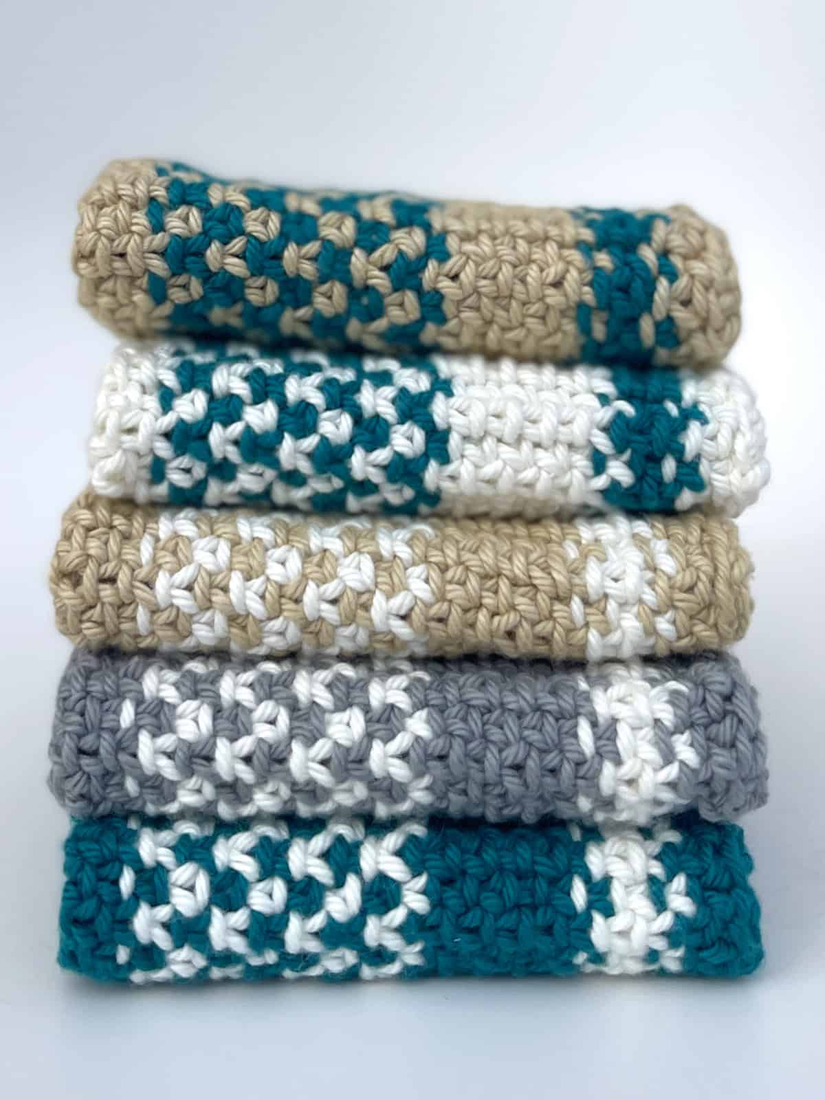 Stack of five knitted dishcloths with blue, white, grey, and tan yarn colors.