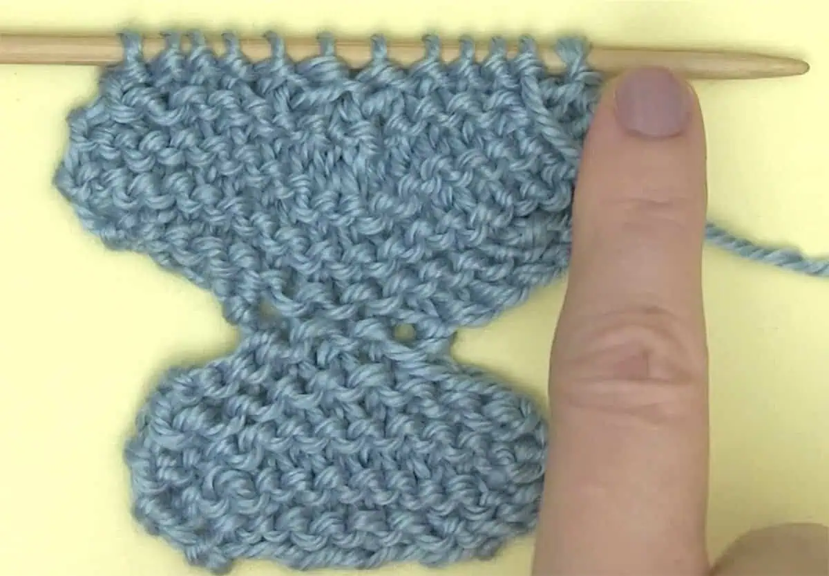 Knitting the body of a butterfly shape flat on straight needle in blue yarn color.