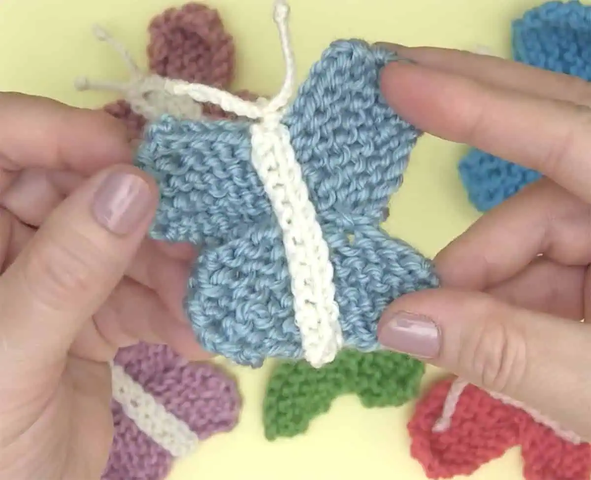 Hands holding a knitted butterfly shape in blue and white yarn colors.