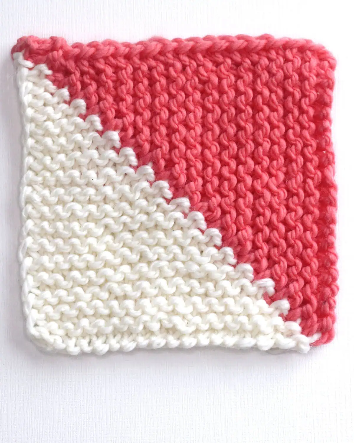 Mitered square half triangle knitted with white and orange colored yarn.