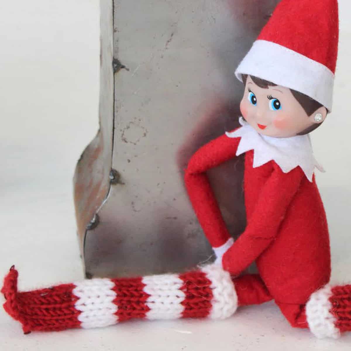 Elf on the Shelf doll wearing a hand knit long boots in red and white yarn colors.