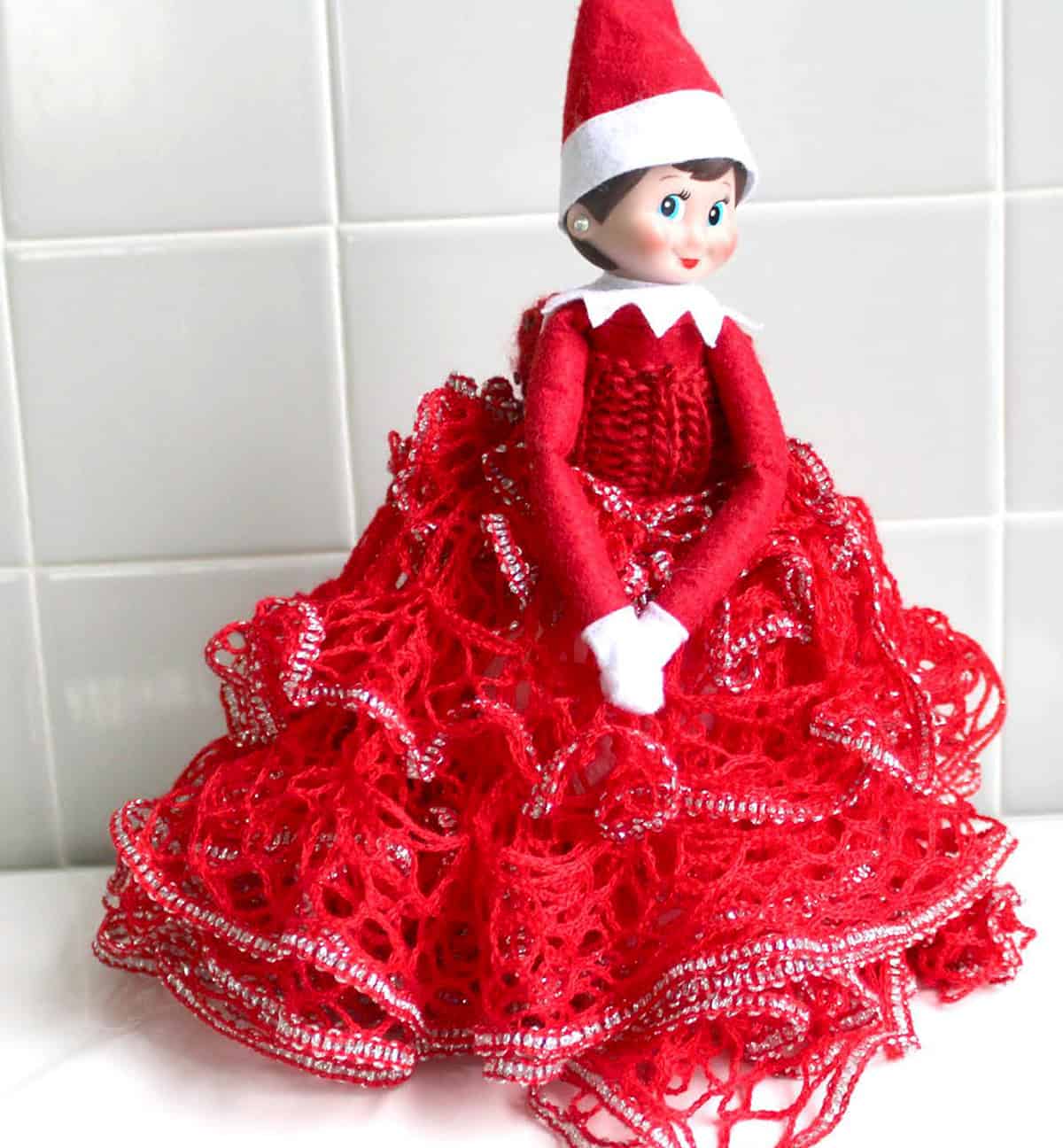 Elf on the Shelf doll wearing a hand knit frilly dress toilet paper cover.