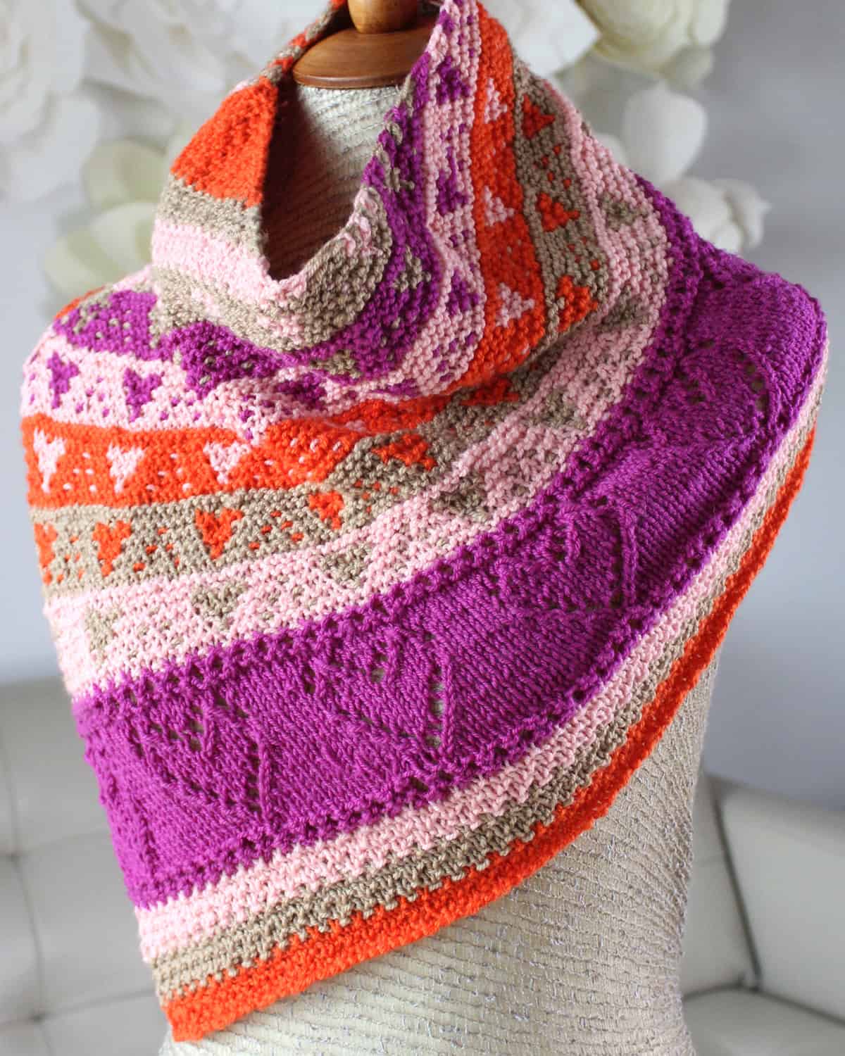 Knitted cowl in orange, pink, and purple yarn colors created with lace and slipped stitch hearts displayed on a mannequin.