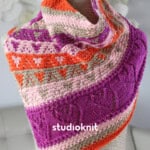 Knitted cowl in orange, pink, and purple yarn colors created with lace and slipped stitch hearts displayed on a mannequin.