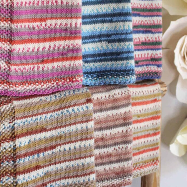 Six knitted baby blankets in colorful fair isle yarn hanging on a blanket ladder.